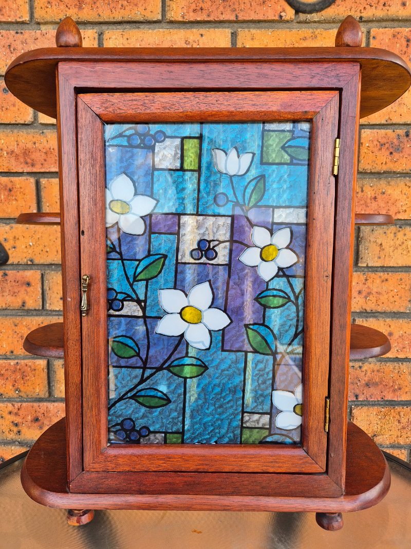 wooden vintage cabinet jewellery box with stained glass widow design sitting on a table.