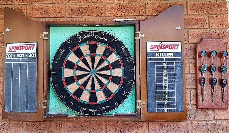 Completed wooden darts holder mounted on outdoor wall holding three sets of darts
