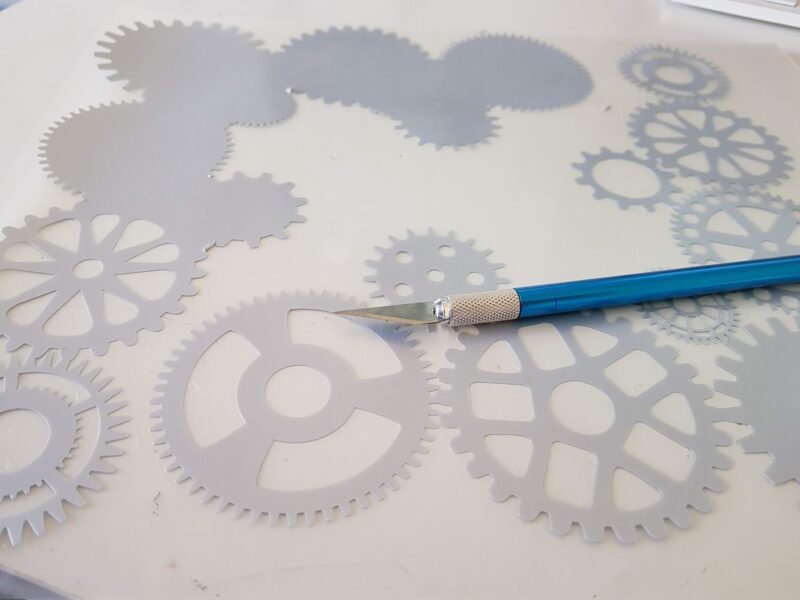 Cricut weeding tool removing excess vinyl from steampunk design on cutting mat