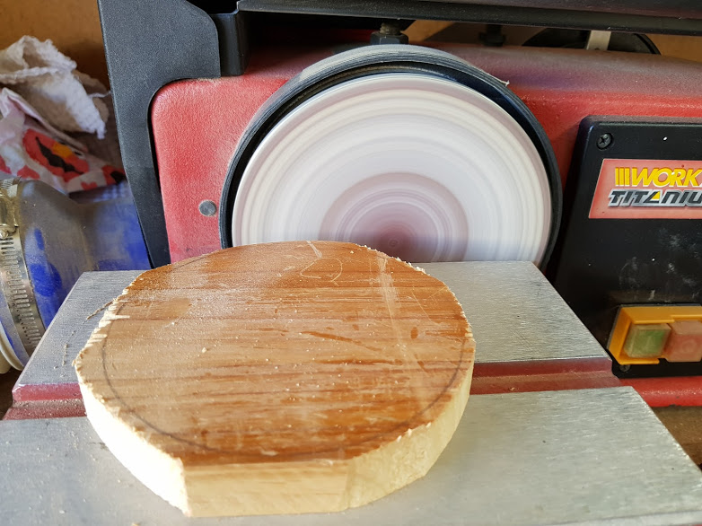 Using a benchtop sander to smooth and shape the wooden tops for candlesticks.