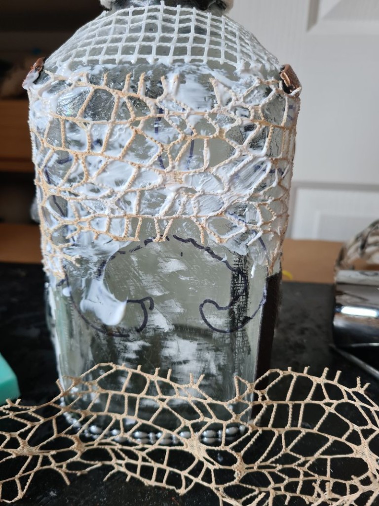 Leather, lace, tapestry mesh, onion bag and zippers arranged for texture on a glass bottle
